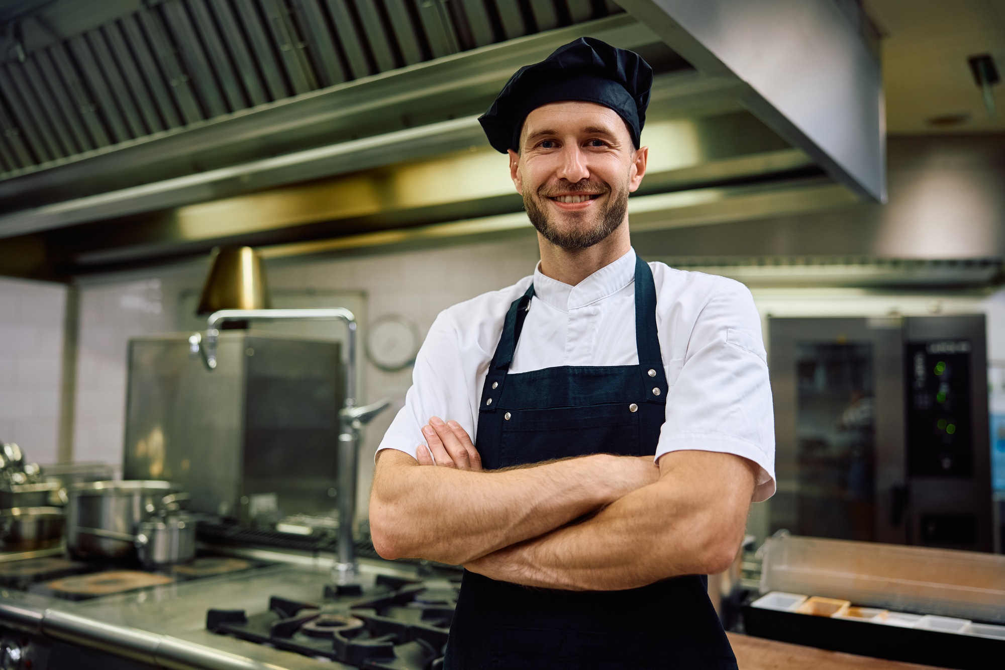 Happy chef with arms crossed in the kitchen looking at camera.